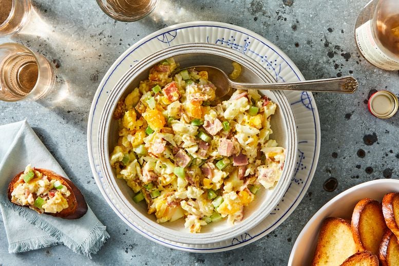 Fried egg salad with chopped onions, celery, and ham in a bowl, with little toasts on the side