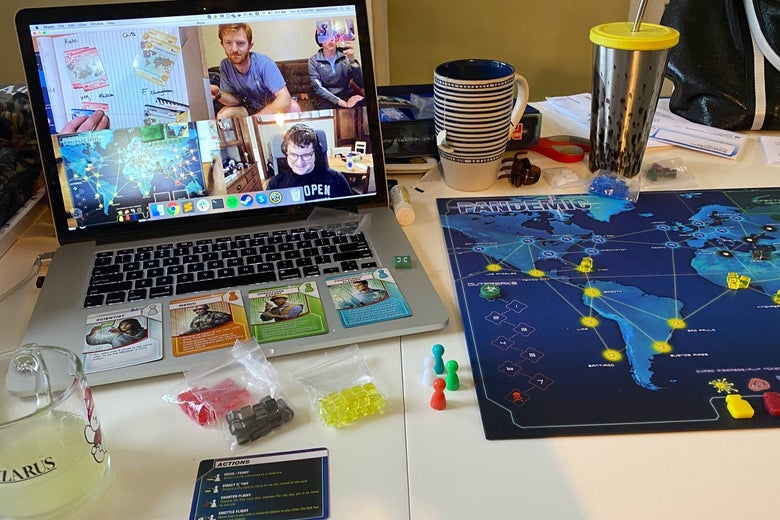 A laptop computer sitting on a table next to a board for the game Pandemic. On the laptop, there's a video conference featuring shots of cards, another Pandemic board, and other players.