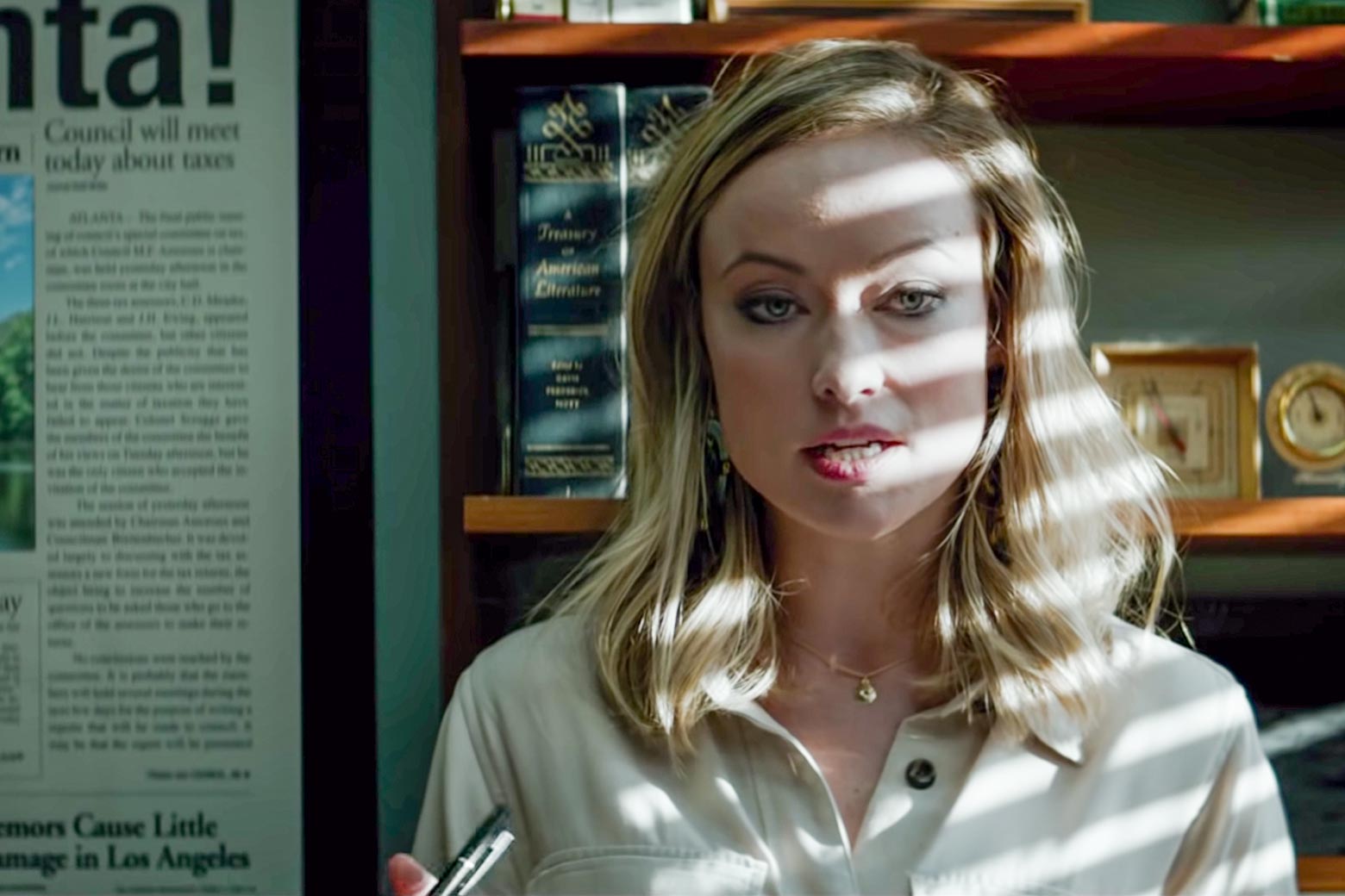 Olivia Wilde stands in the shadow of half-opened window blinds as Kathy Scruggs in this still from Richard Jewell