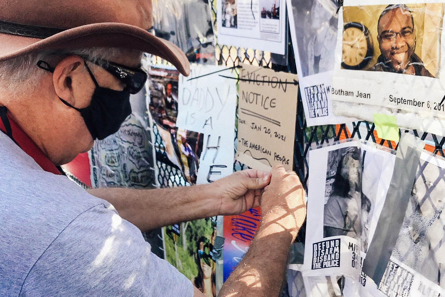 A man posts a sign that says "EVICTION NOTICE" on a fence covered in fliers and photographs.