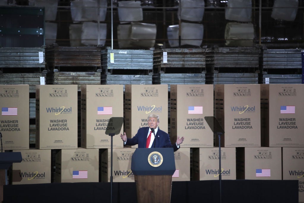 Trump gives a speech against a backdrop of boxed-up washing machines and stacks of what appear to be metal sheets.