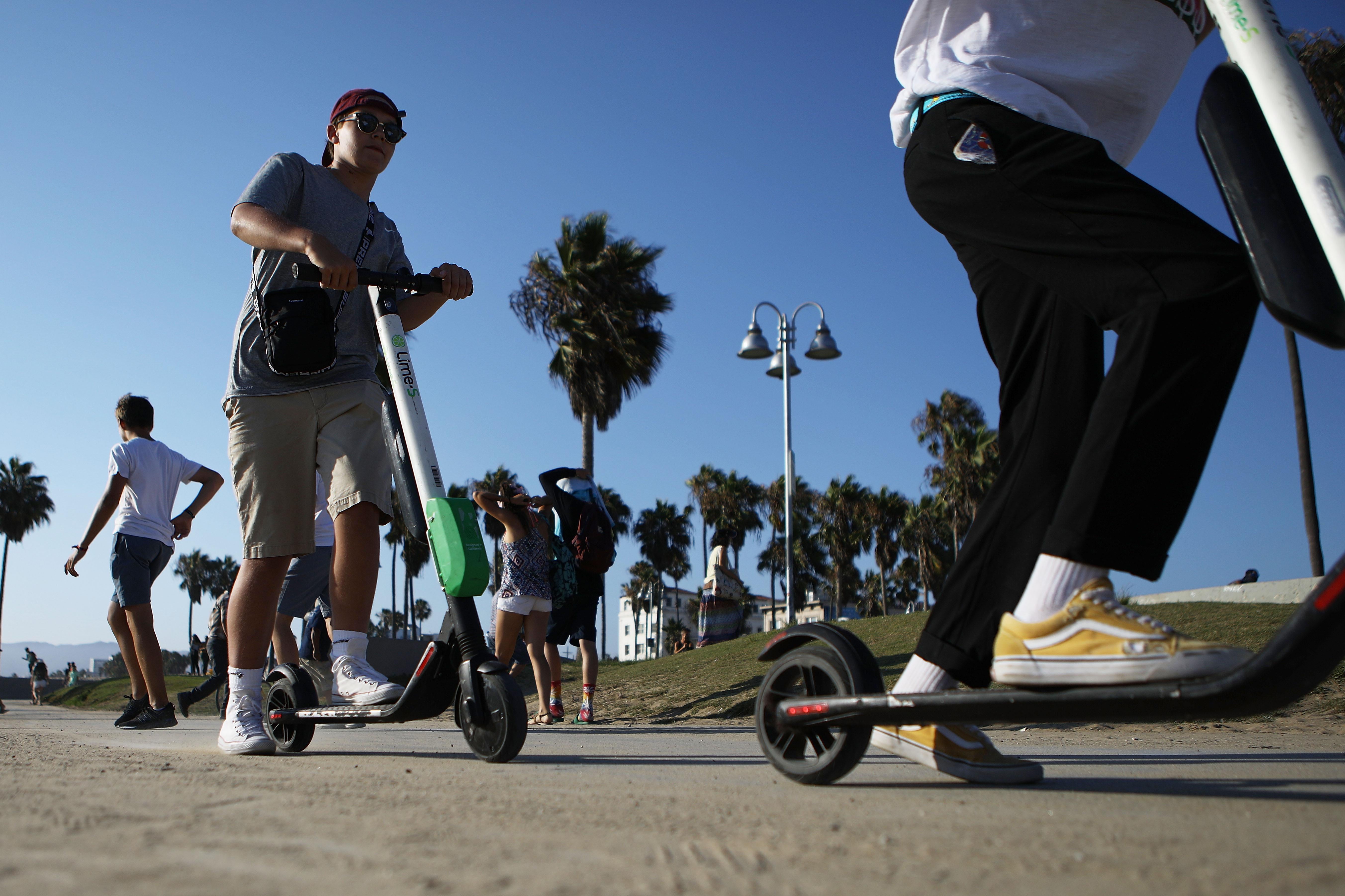 Two people ride Lime shared dockless electric scooters along Venice Beach on August 13, 2018 in Los Angeles, California. 