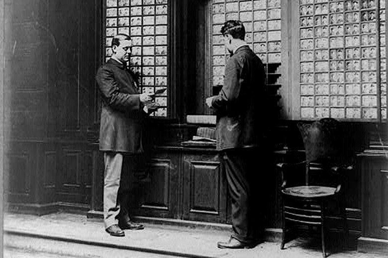 Two men look over photos of criminal in the NYPD's rogue's gallery in July of 1909.
