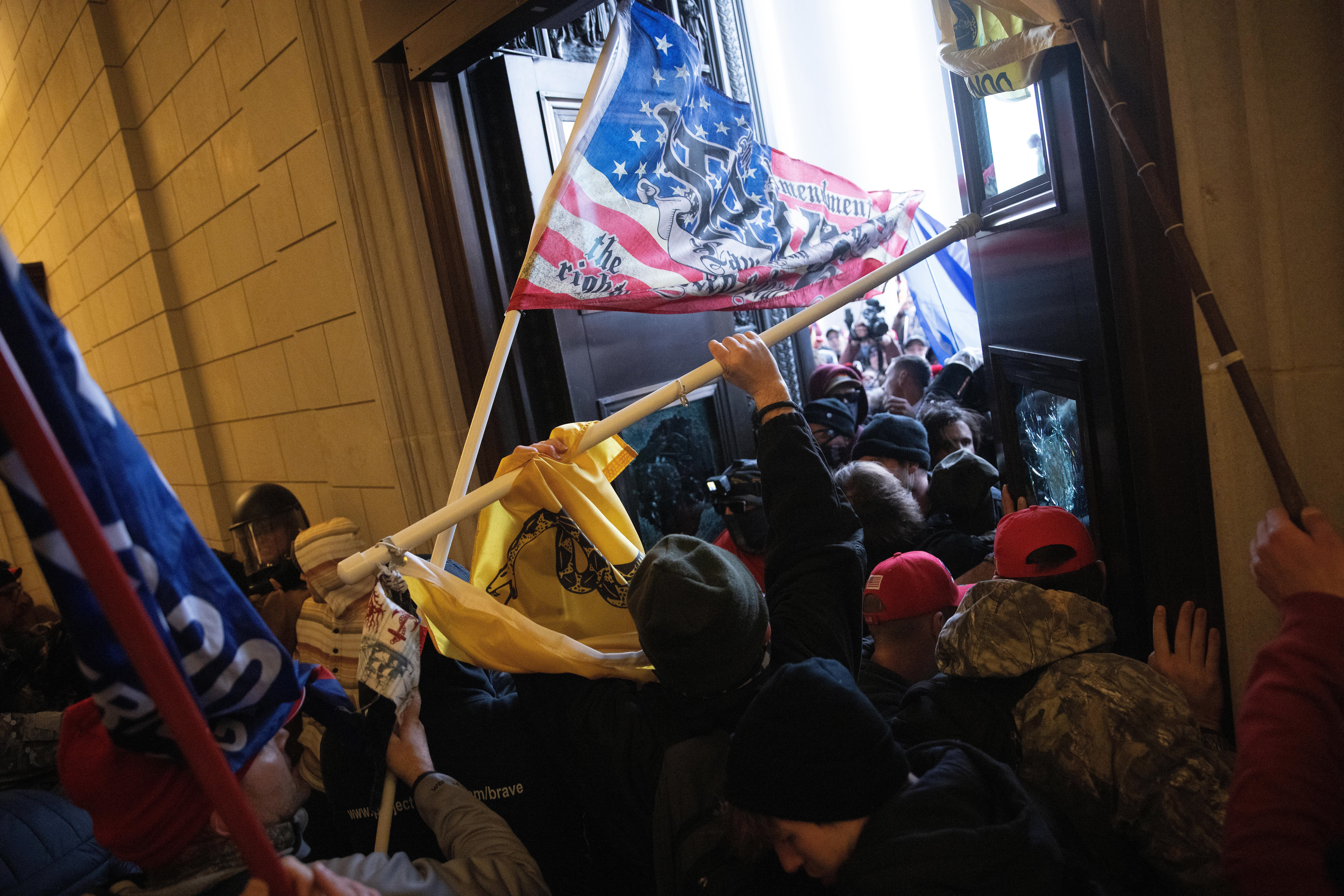 A mob of people carrying U.S. and Gadsden flags enters the Capitol building.