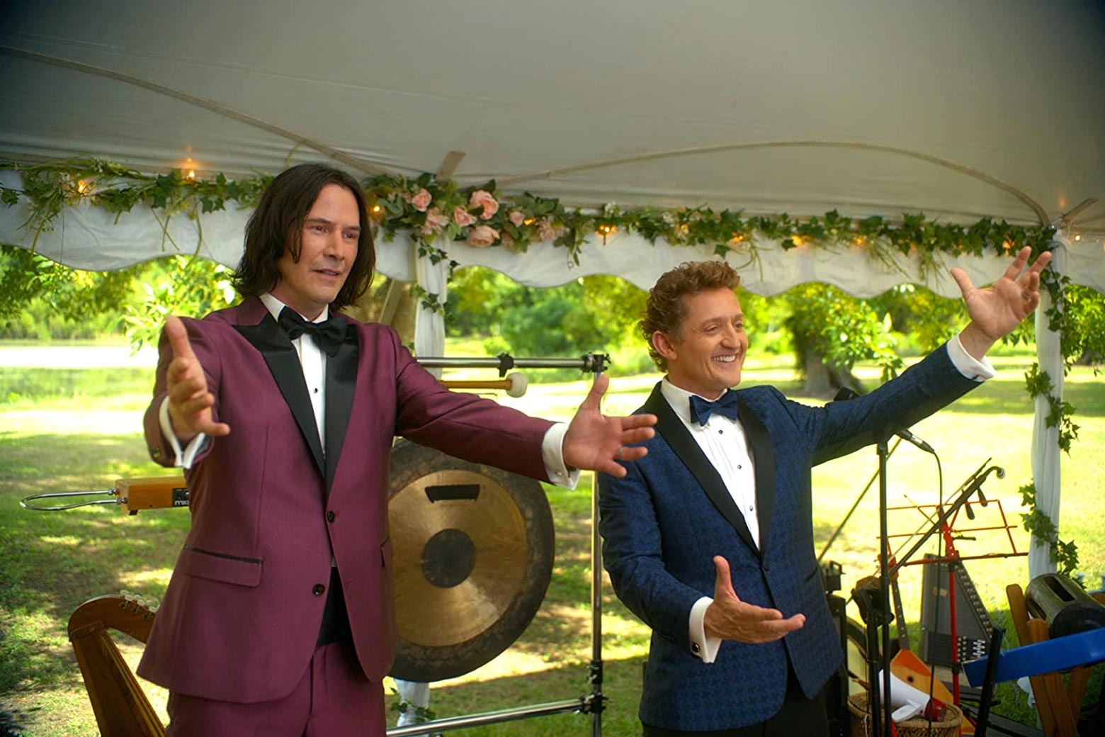 Keanu Reeves and Alex Winter stand in front of a gong and stretch out their hands in a scene from in Bill & Ted Face the Music