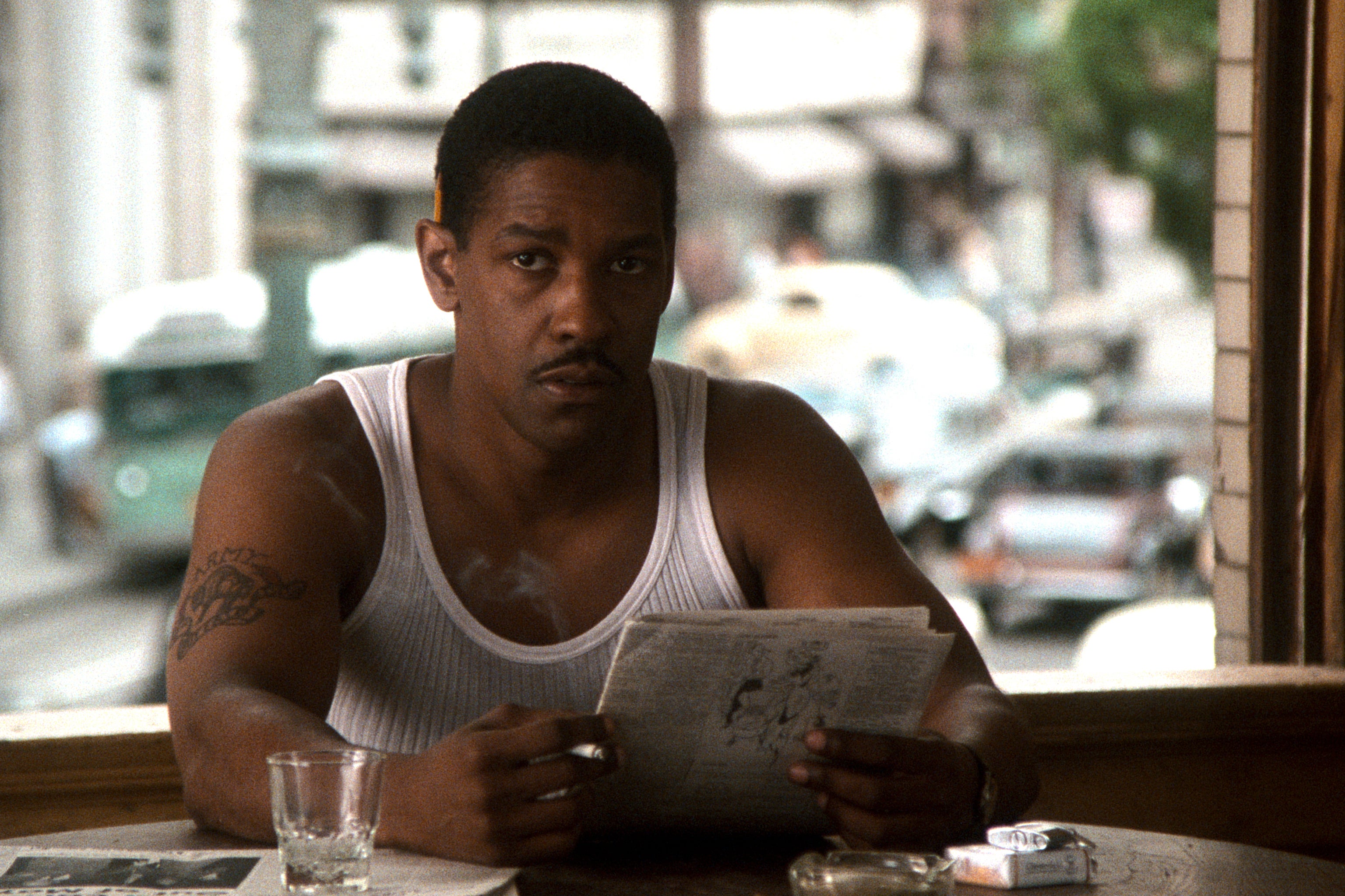 Denzel Washington looking up from reading a newspaper.