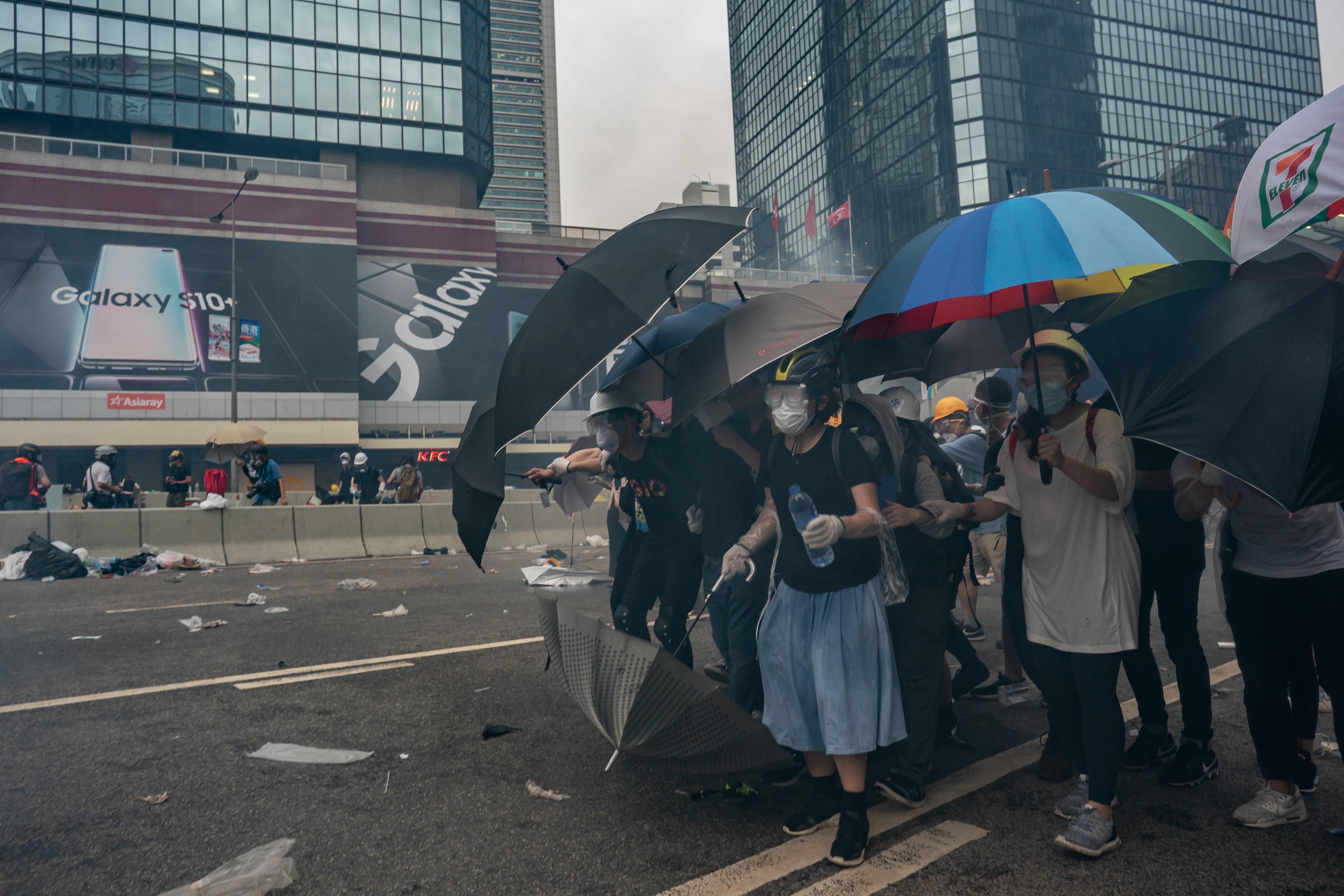 Protesters hold umbrellas as teargas is fired.