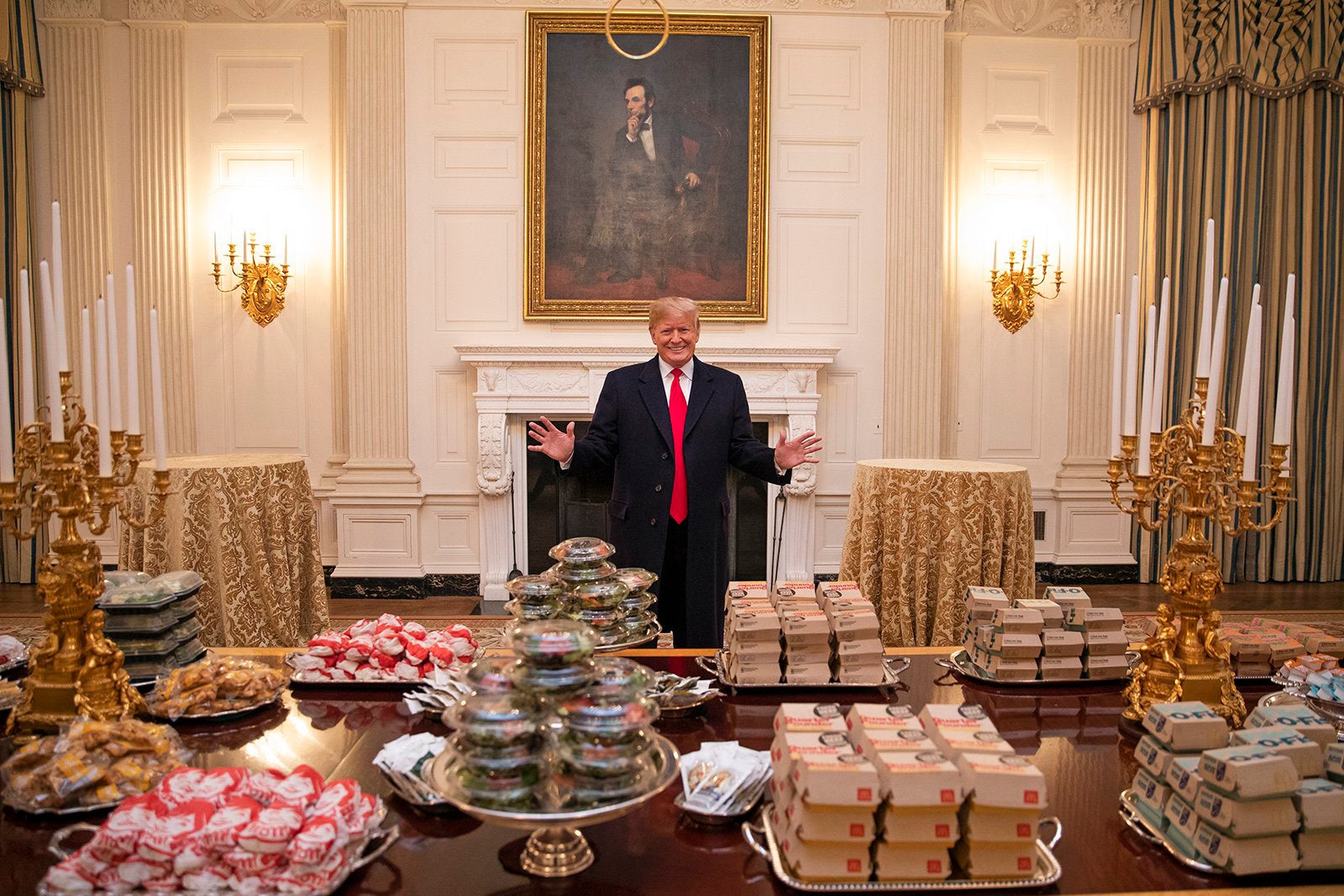 Donald Trump presides over a banquet table overflowing with fast food.