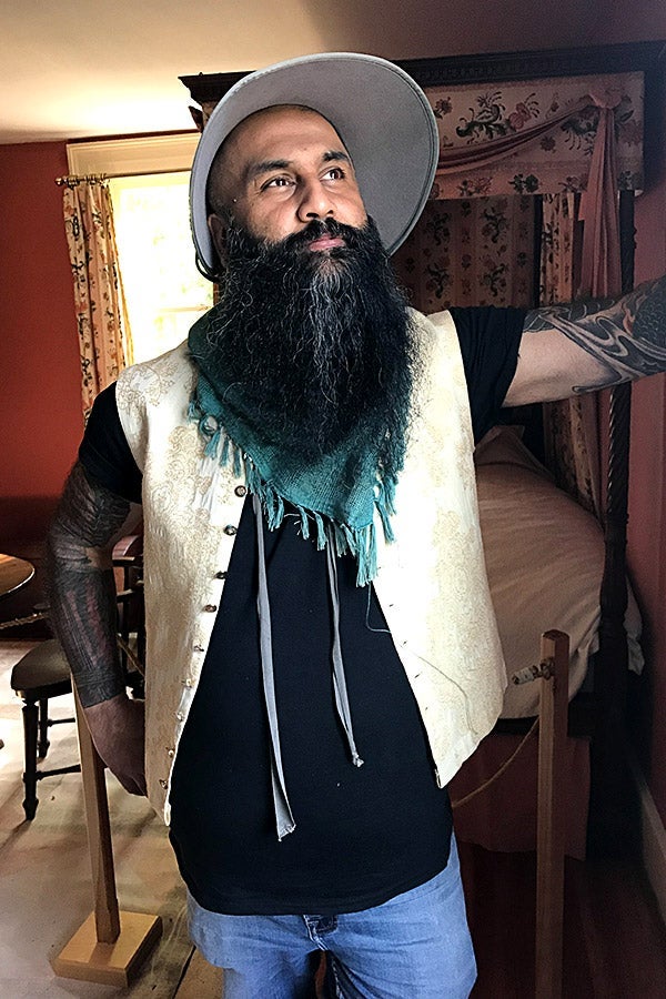 Hasan Hai, with a long black-and-white beard, stands in his home. 