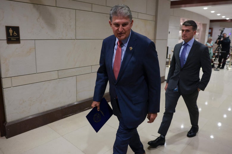 Sen. Joe Manchin walking in the U.S. Capitol. He's holding a document and wearing a blue suit.