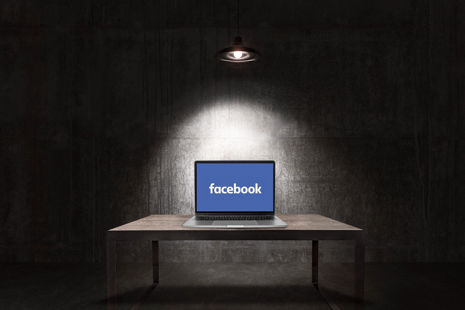 A laptop, open to a screen that shows the word Facebook on a blue background, sits on a table in a darkened interrogation room.