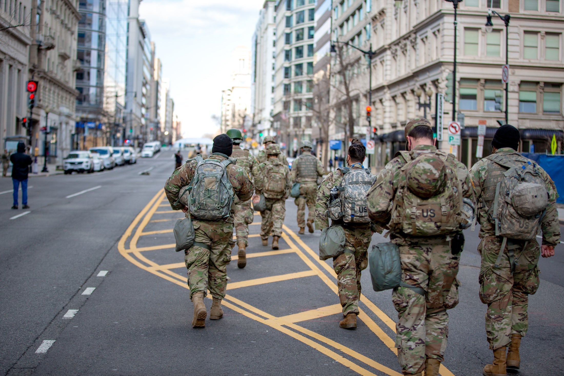 National Guard members in camo walk away from the camera in the middle of an empty street
