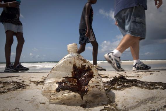 Beachgoers walk past a bottle coated with oil from the Deepwater Horizon oil spill in Pensacola Beach, Florida