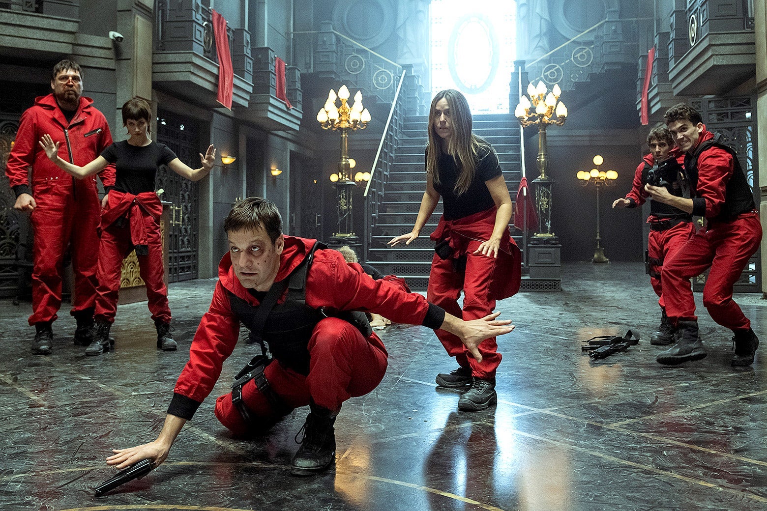 Five thieves in red jumpsuits spread out across the inside of a bank.