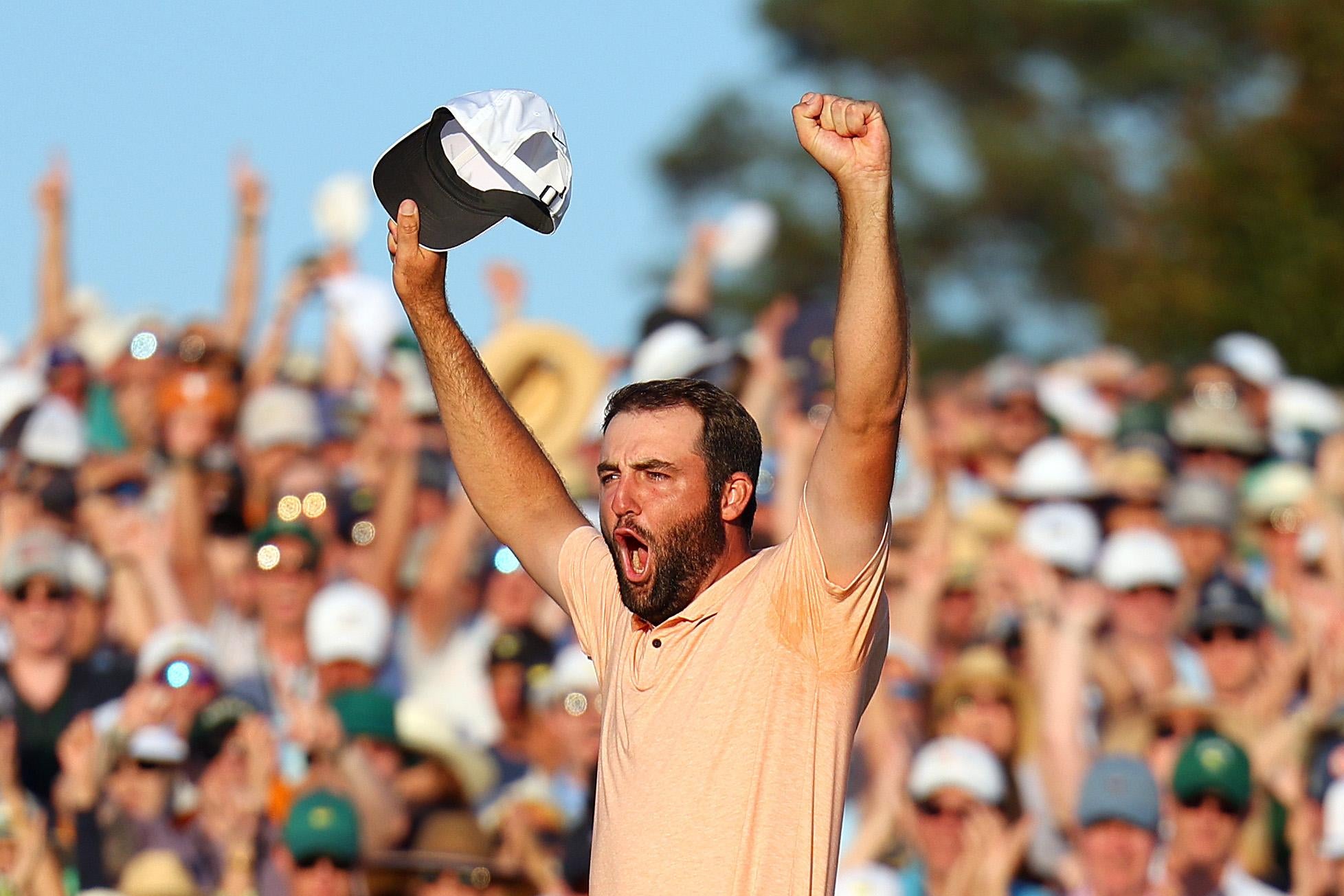 Scheffler raises both his arms, his left in a fist and right clutching a cap, and whoops as the crowd behind him applauds.