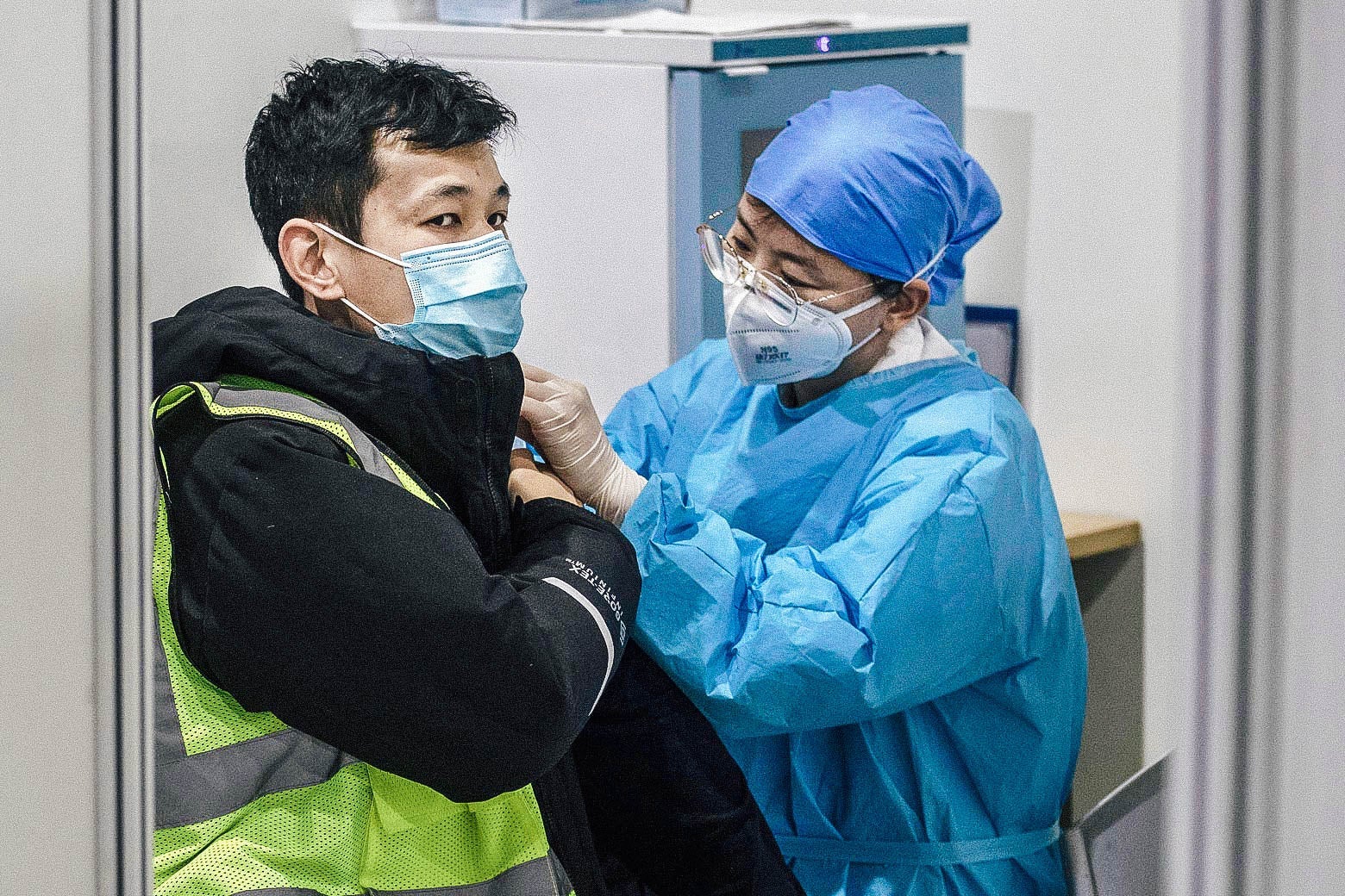 A person in protective gear gives a man in a mask a vaccine.