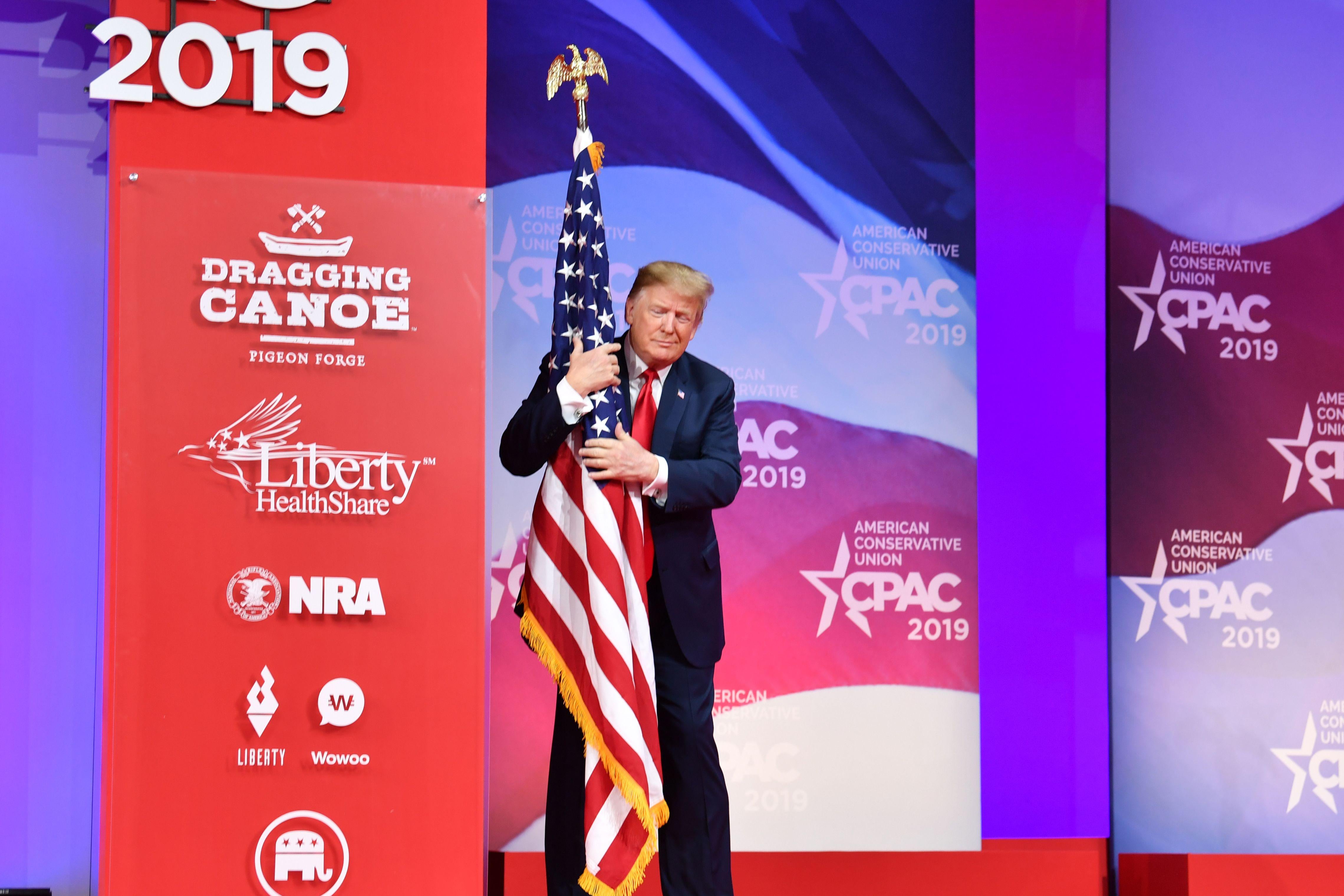 President Donald Trump hugs the U.S. flag as he arrives to speak at the annual Conservative Political Action Conference (CPAC) in National Harbor, Maryland, on March 2, 2019.