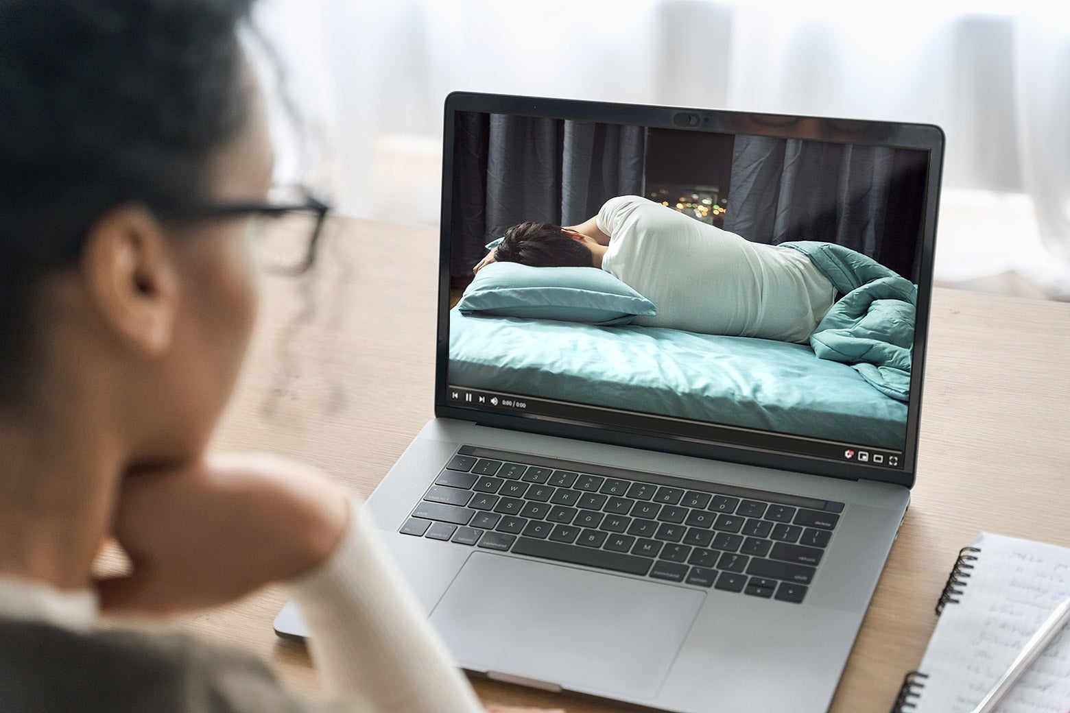 A person watches a man sleeping on a laptop.