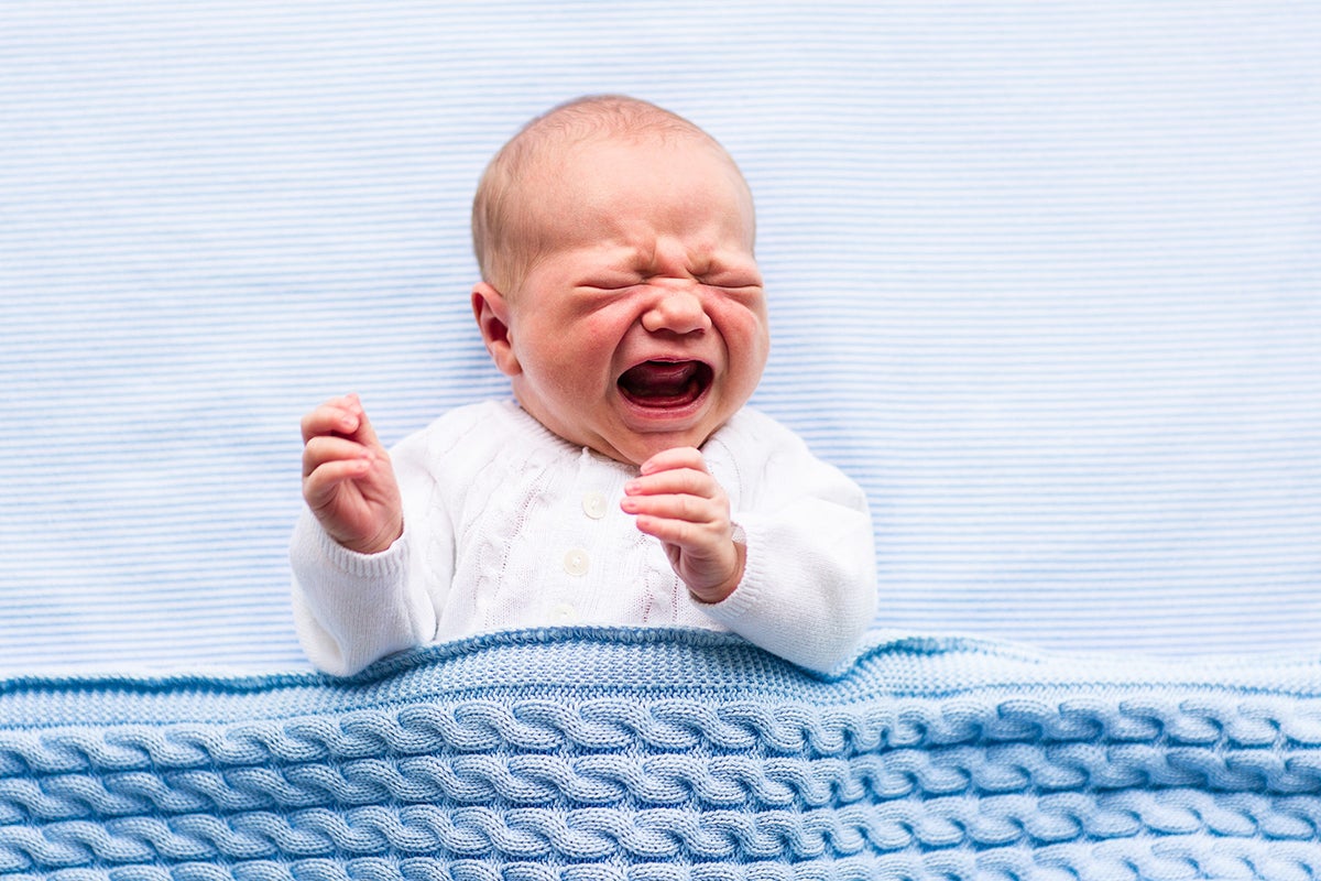 A small baby is in their crib crying and upset