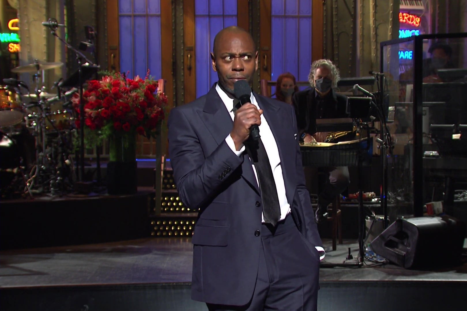 Dave Chappelle, in a blue suit, on SNL's main stage, holding a microphone.