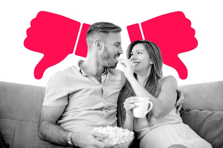 Woman feeding a man a kernel of popcorn on a couch.