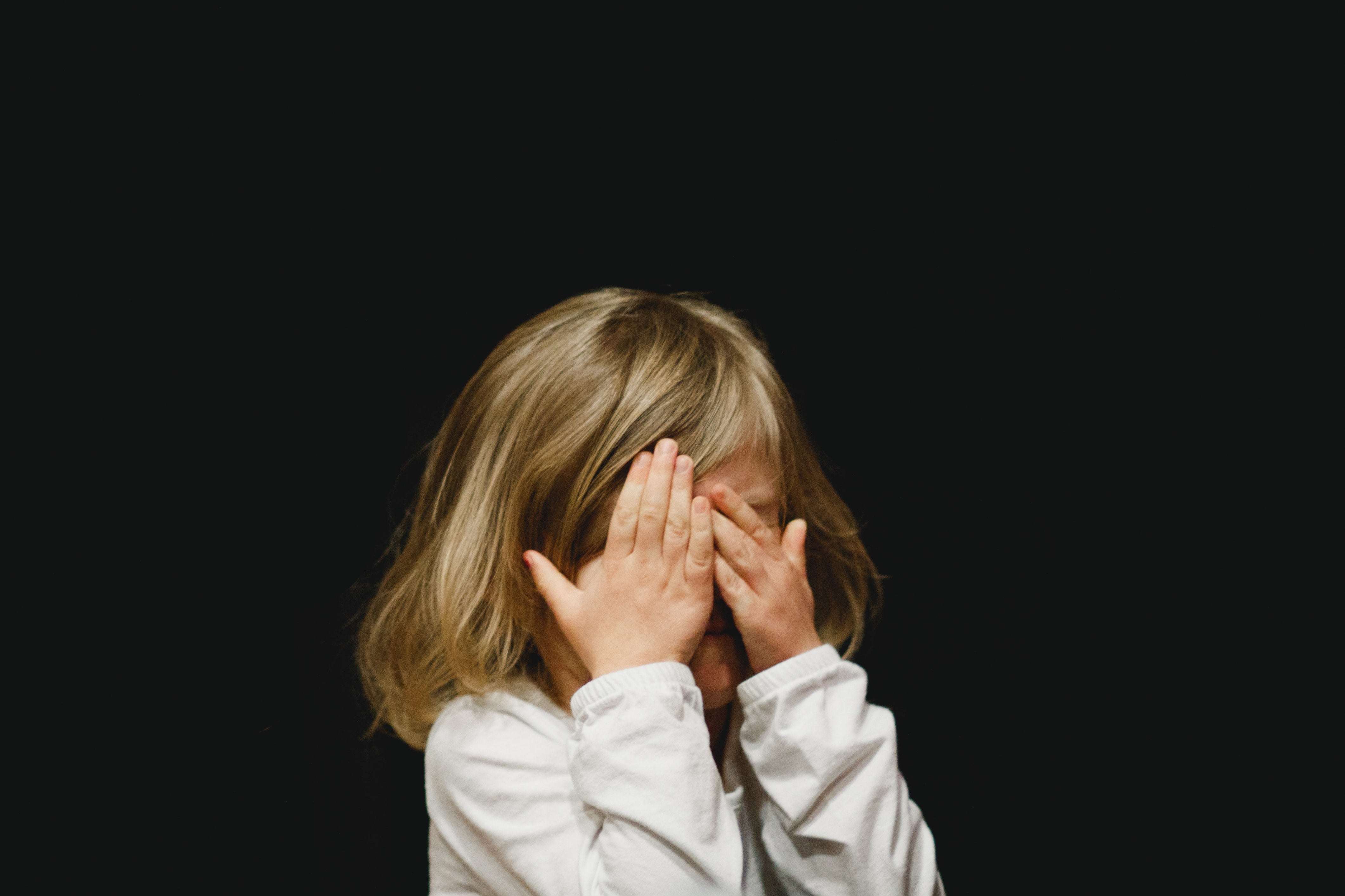 A small child covering her face with her hands. 