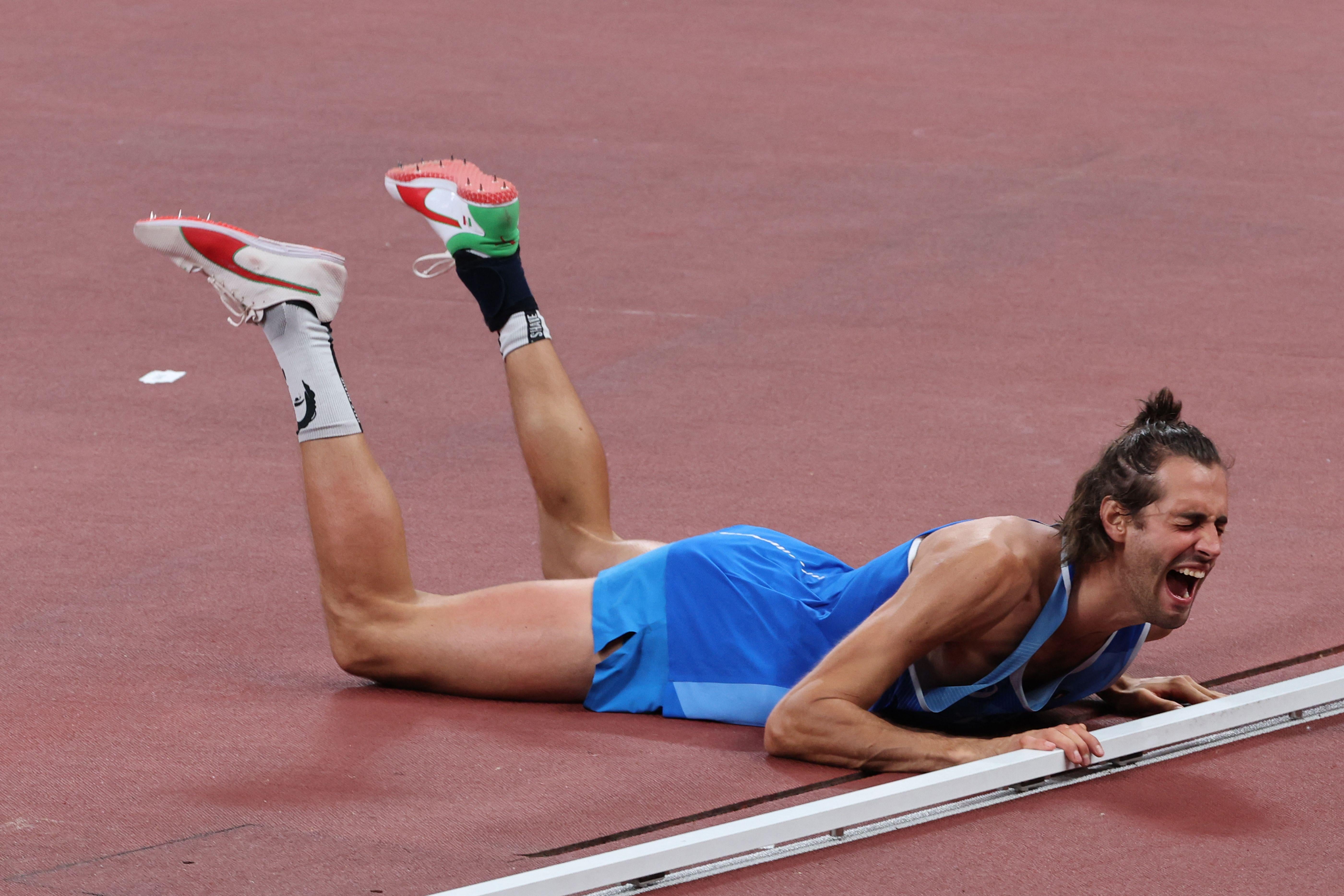 A tall, lanky high jumper lies belly-down on the ground, his legs raised behind him, screaming.