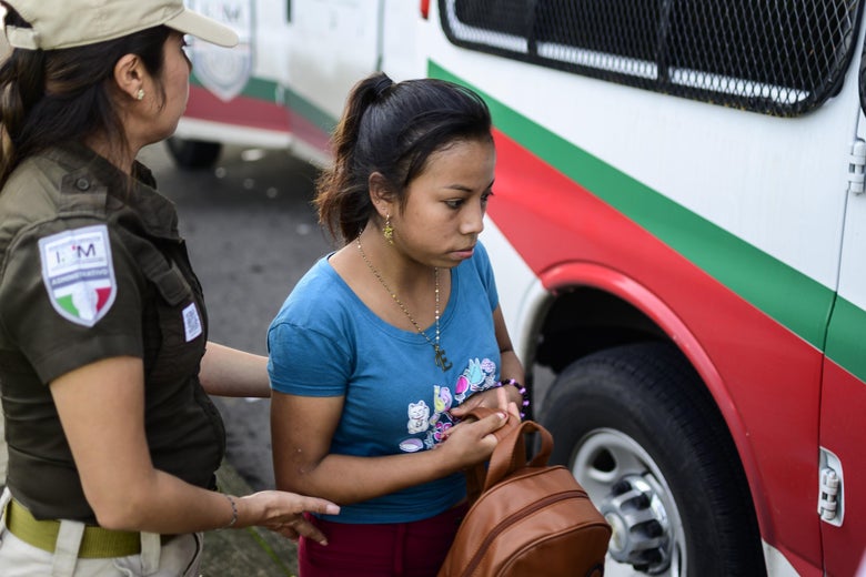 A migrant woman carrying a backpack, being detained next to a bus.