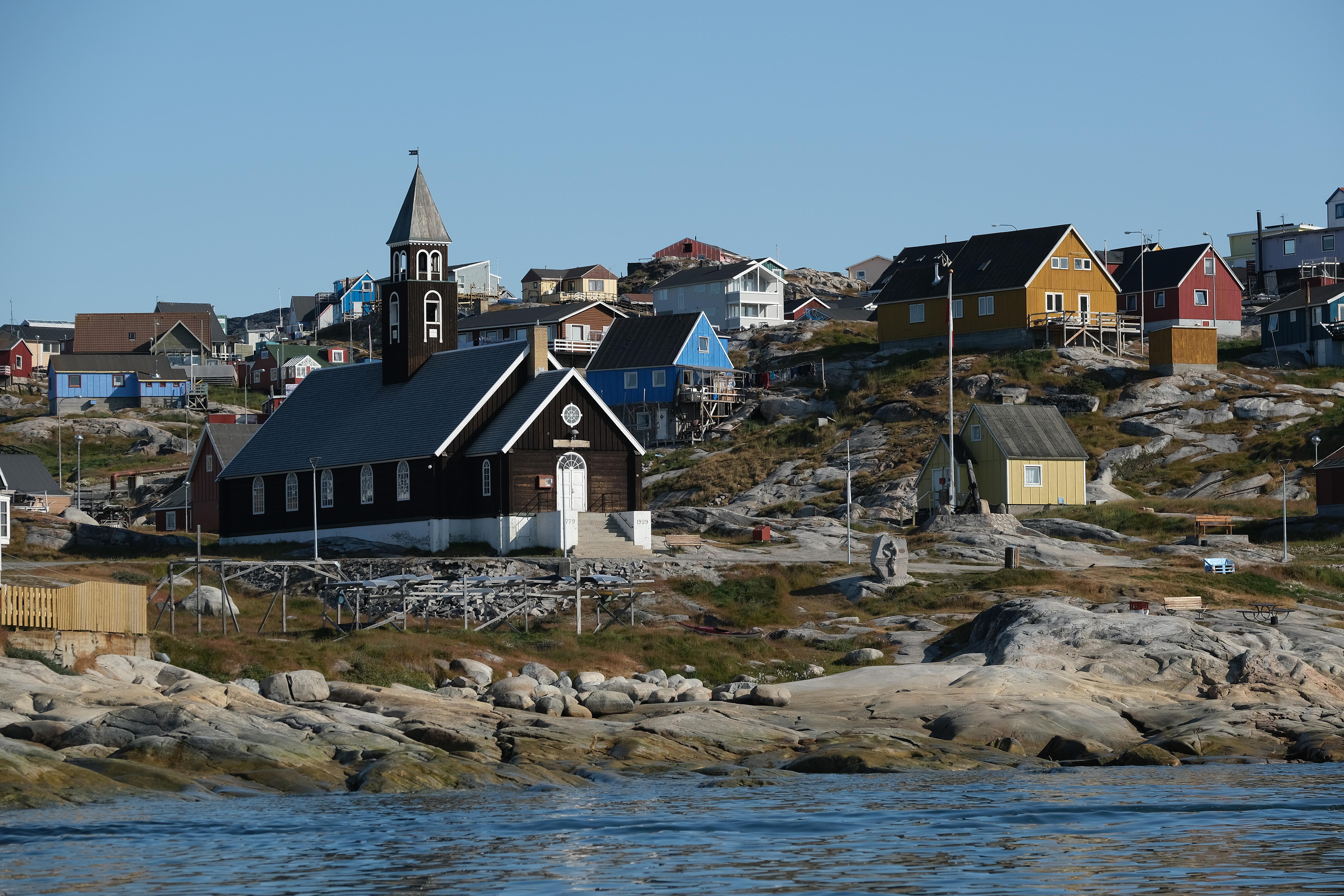 A church and a cluster of colorful buildings near a rocky beach.