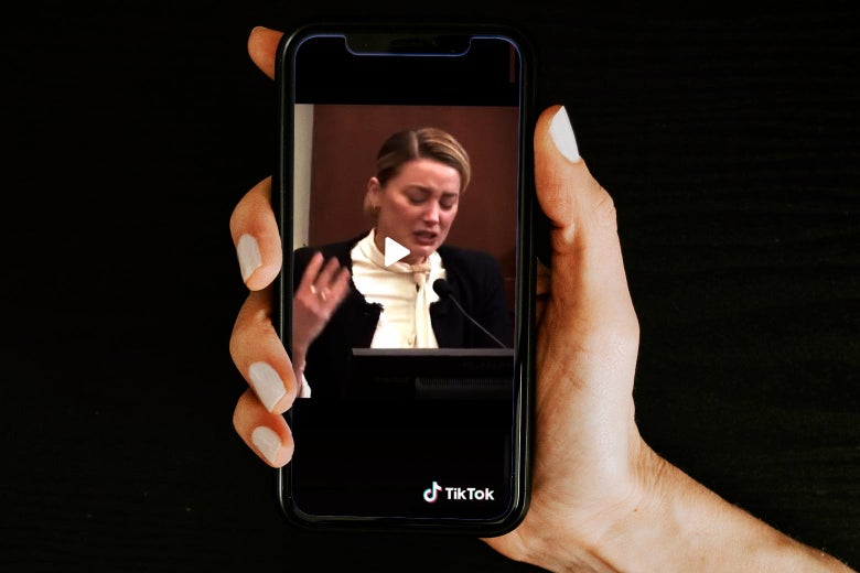 Hand holding a phone displaying a TikTok video of Amber Heard sobbing on the witness stand