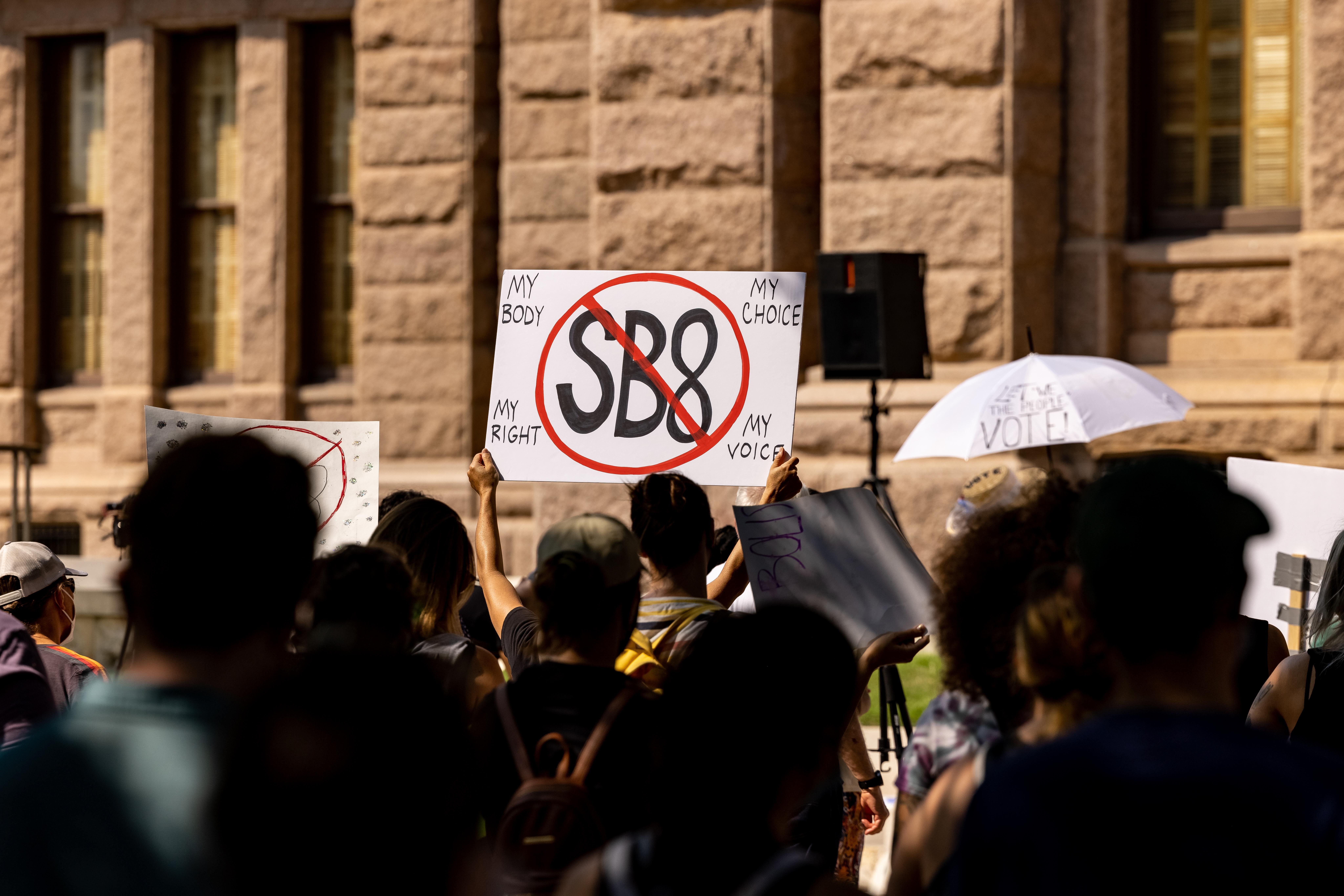 Abortion rights activists rally at the Texas State Capitol on September 11, 2021 in Austin, Texas — one holds a sign with SB 8 crossed out.