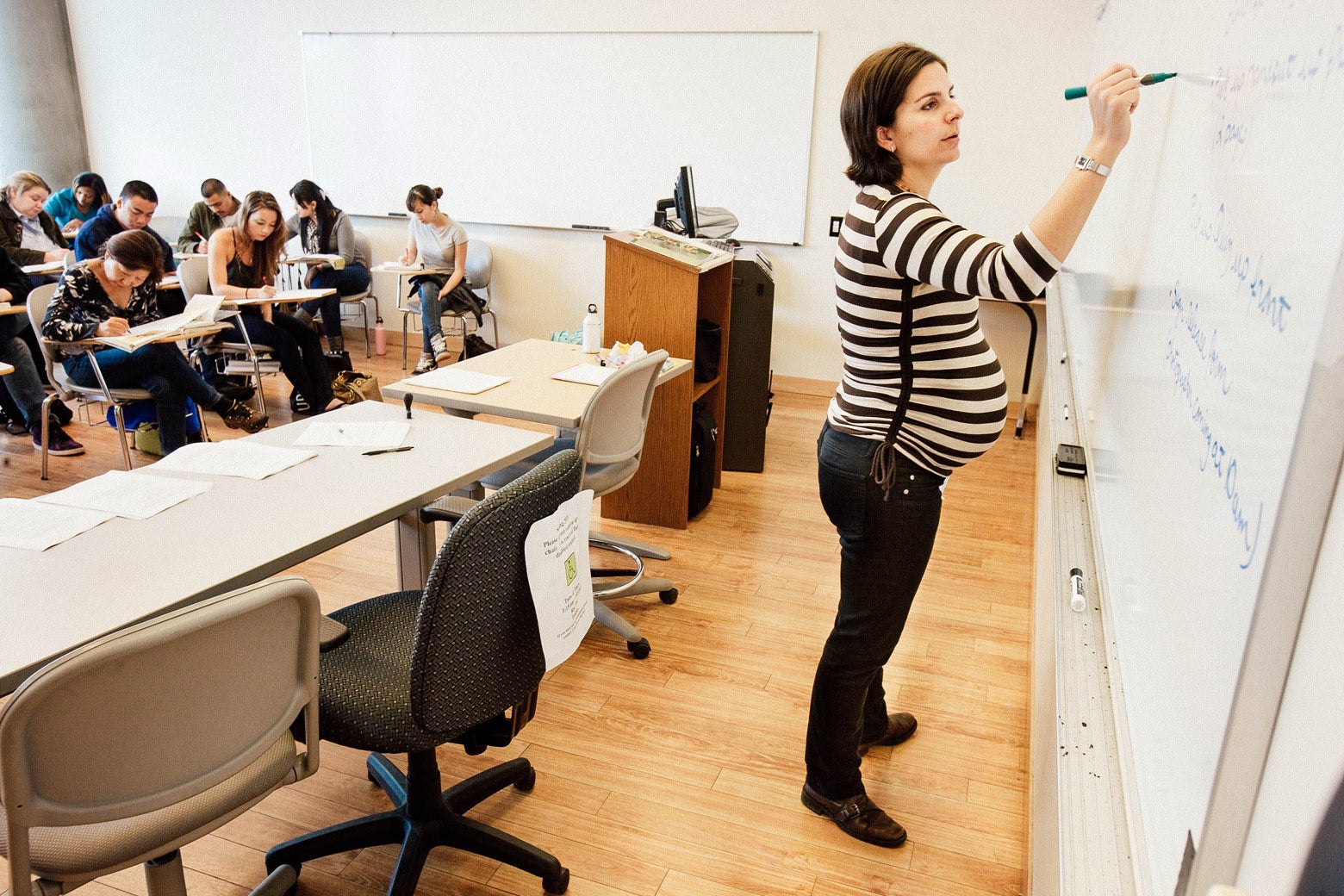 Rebecca writes on a whiteboard in front of a classroom of students.