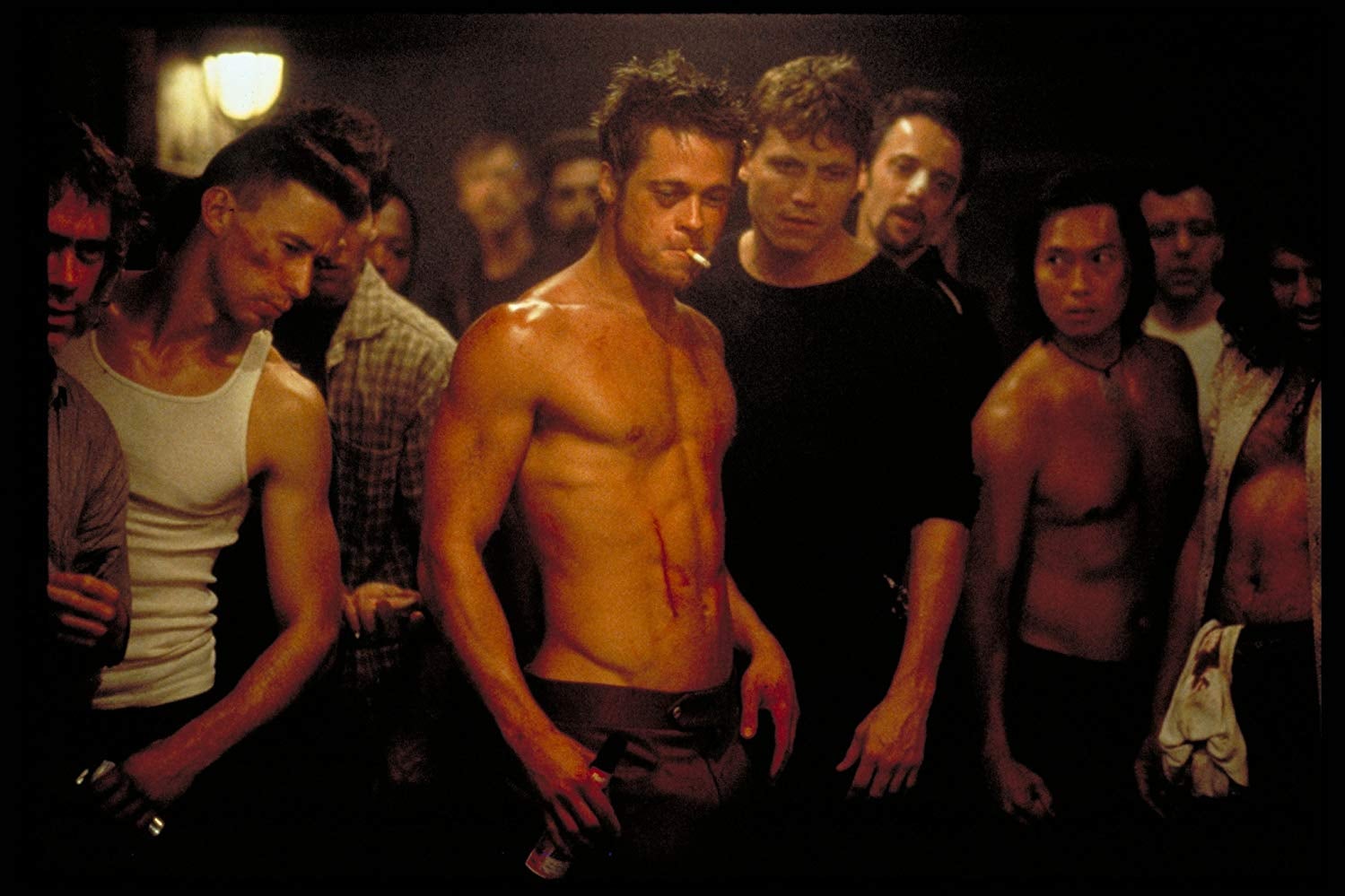 Brad Pitt stands shirtless in a crowd of bruised and bloodied men. A cigarette dangles between his lips.