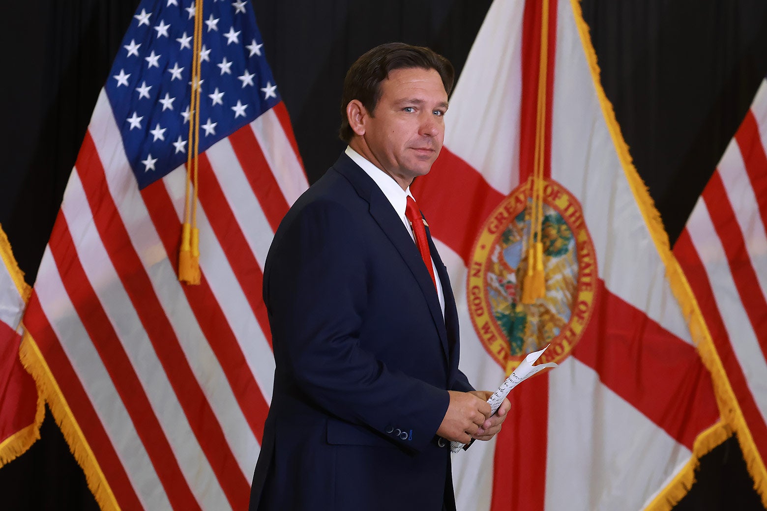 DeSantis holds papers, standing in front of Florida's flag and the U.S. flag.