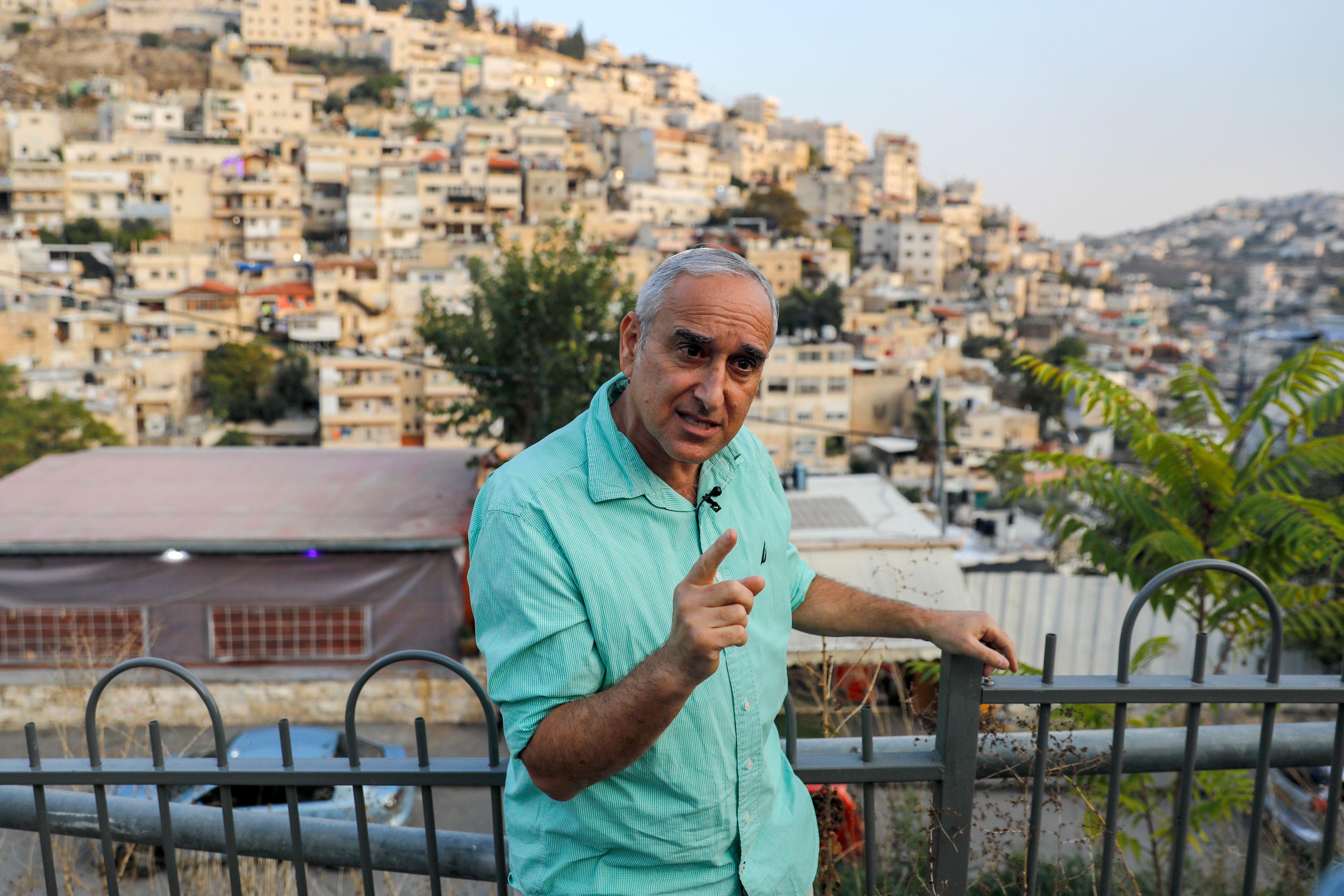 Luria speaks, his pointer finger raised, with the homes on hills of the neighborhood behind him in the background.