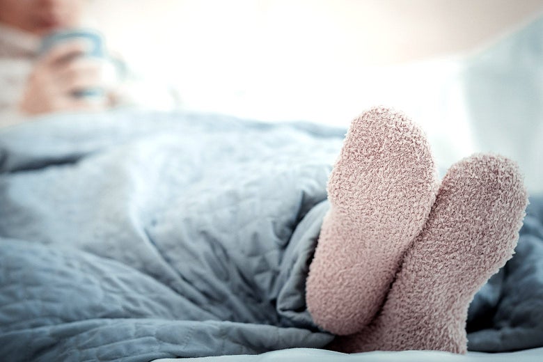 A woman lying in bed with her fuzzy socks sticking out of the covers