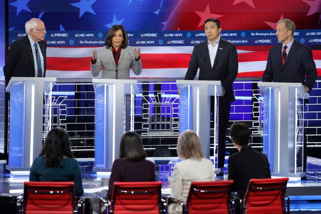 Harris speaks as three other candidates are pictured looking on. The backs of the four debate moderators are seen in the foreground.