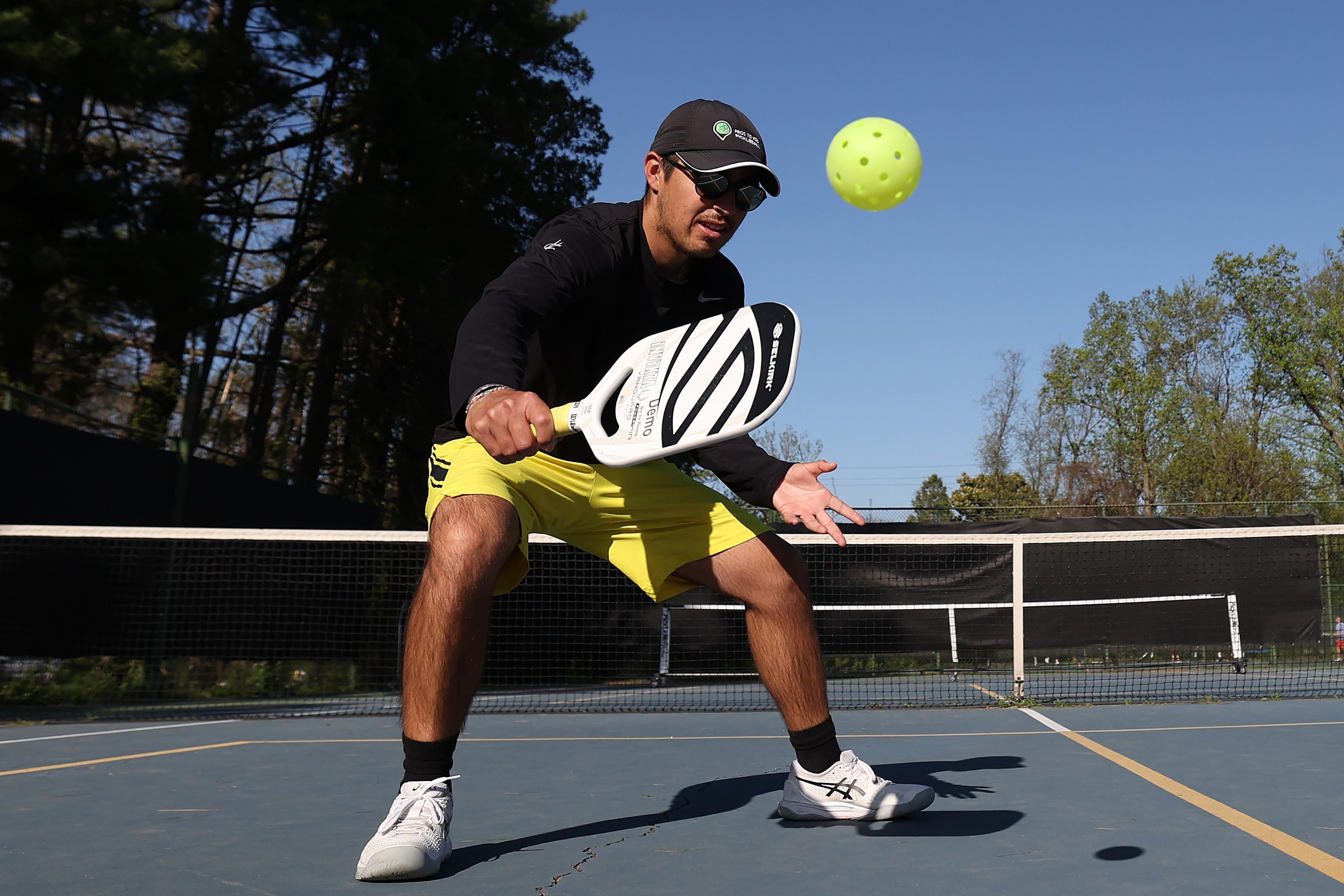 A man bends his knees, holding out a paddle to hopefully make contact with a plastic ball with holes.