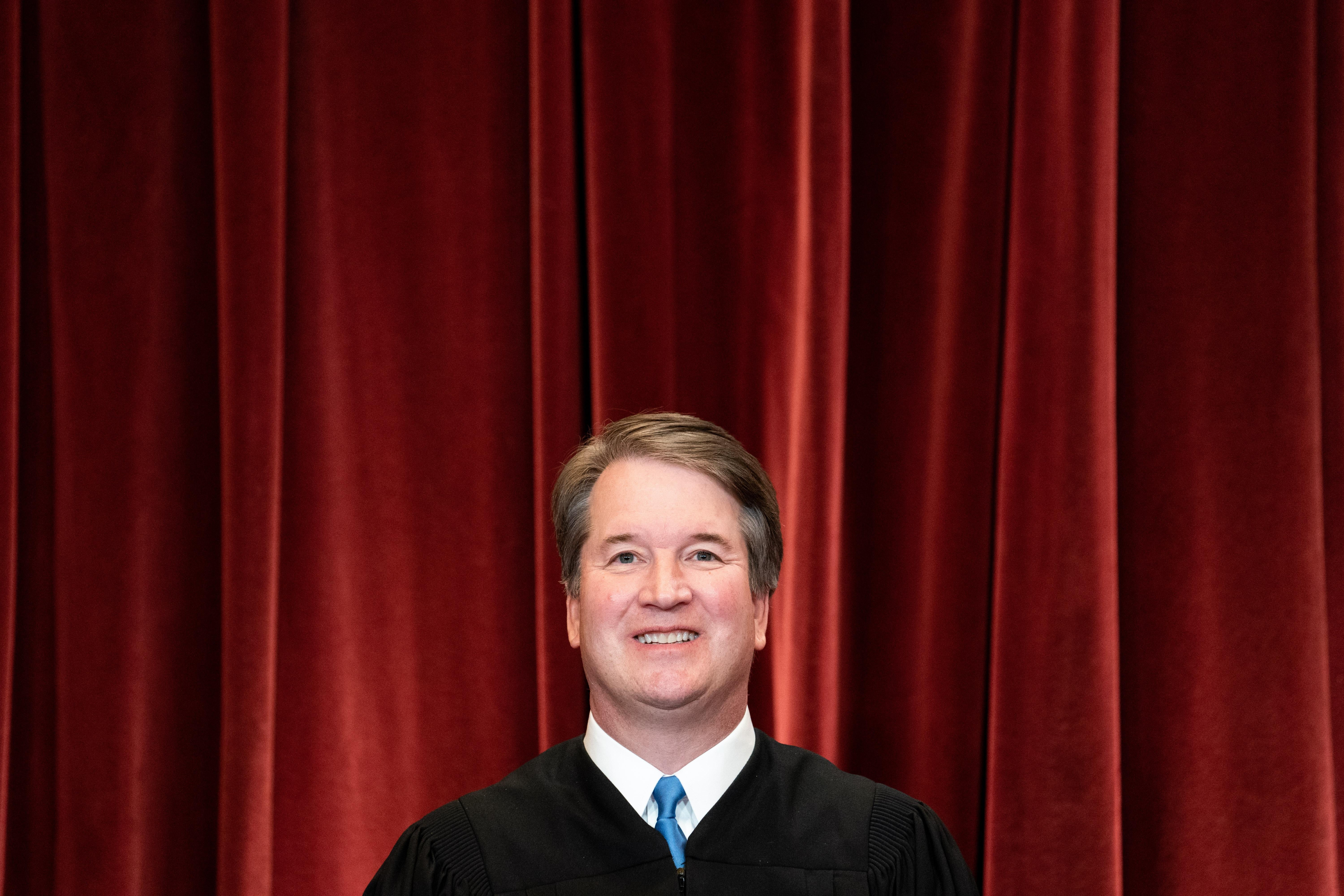 Kavanaugh smiling in his robes in front of a red curtain