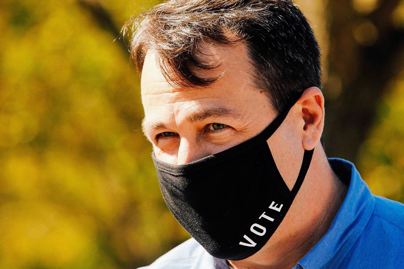 Cal Cunningham wears a blue collared shirt and a black face mask that says "vote" on it.