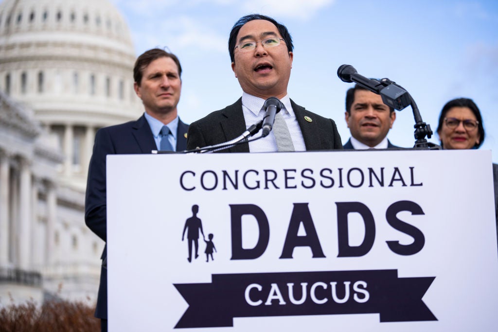 With the Capitol and three colleagues behind him, New Jersey Rep. Andy Kim speaks into a lectern that has a "Congressional Dads Caucus" poster on its front.