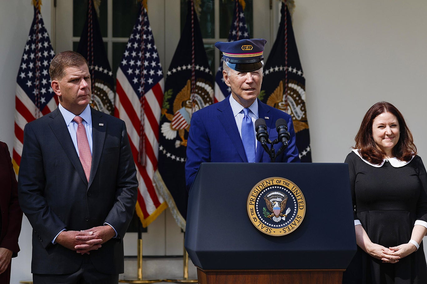 Joe Biden in the Rose Garden, wearing a train conductor cap, surrounded by Marty Walsh and Celeste Drake