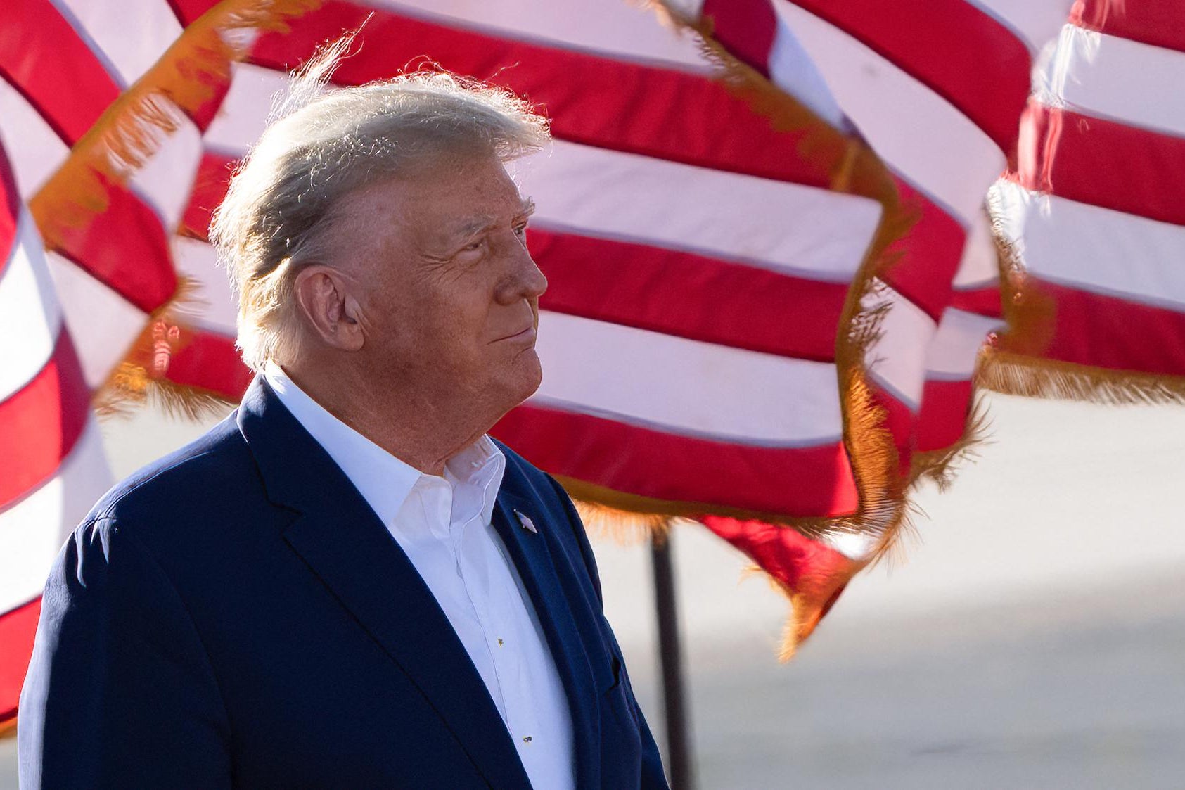 Trump, in profile, is seen squinting toward the sun while standing in front of American flags. 