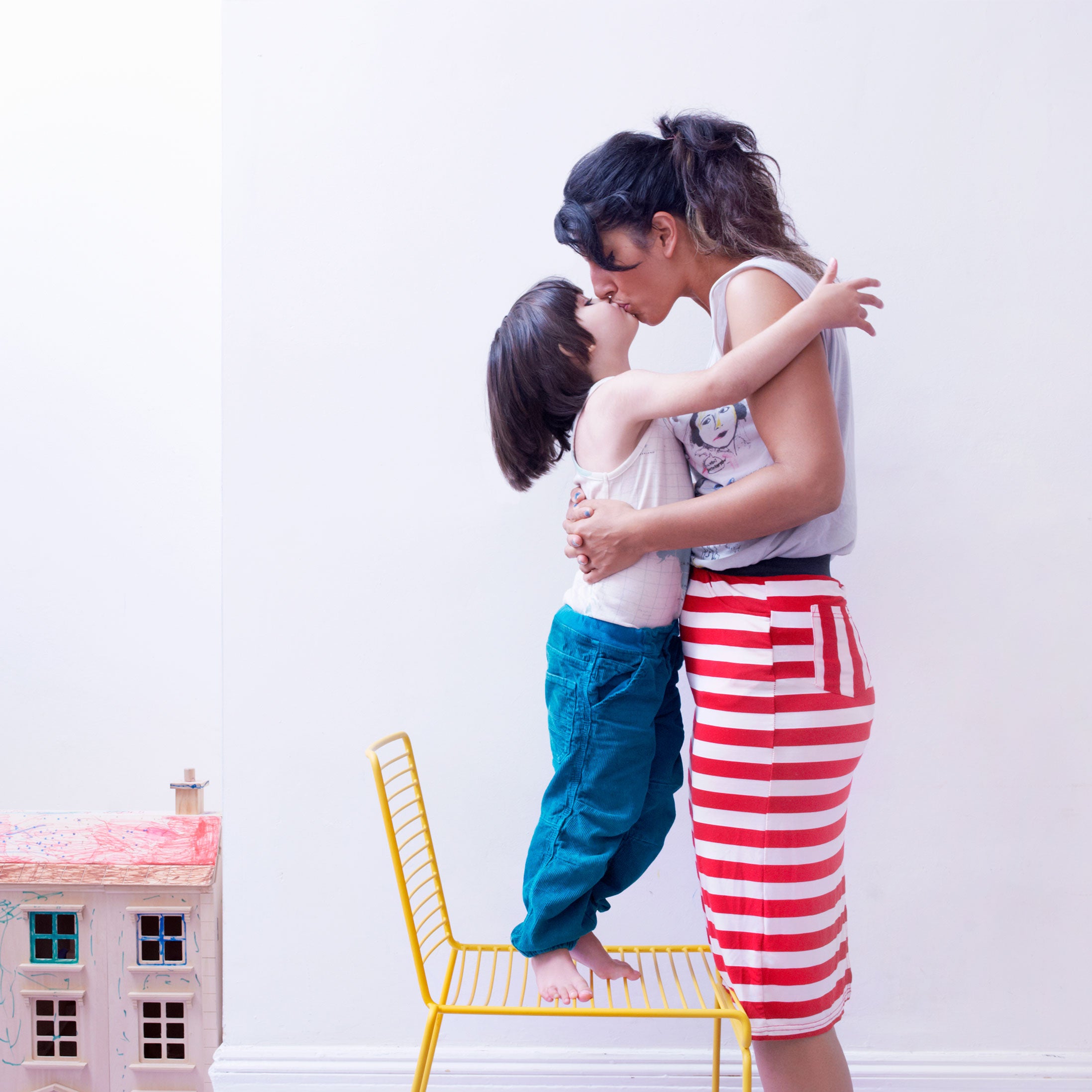 Young child standing on a chair smooching his mom.