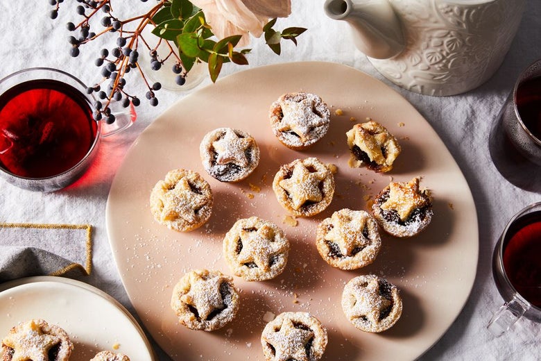 11 miniature mince pies on a blush pink plate with star-shaped crusts.