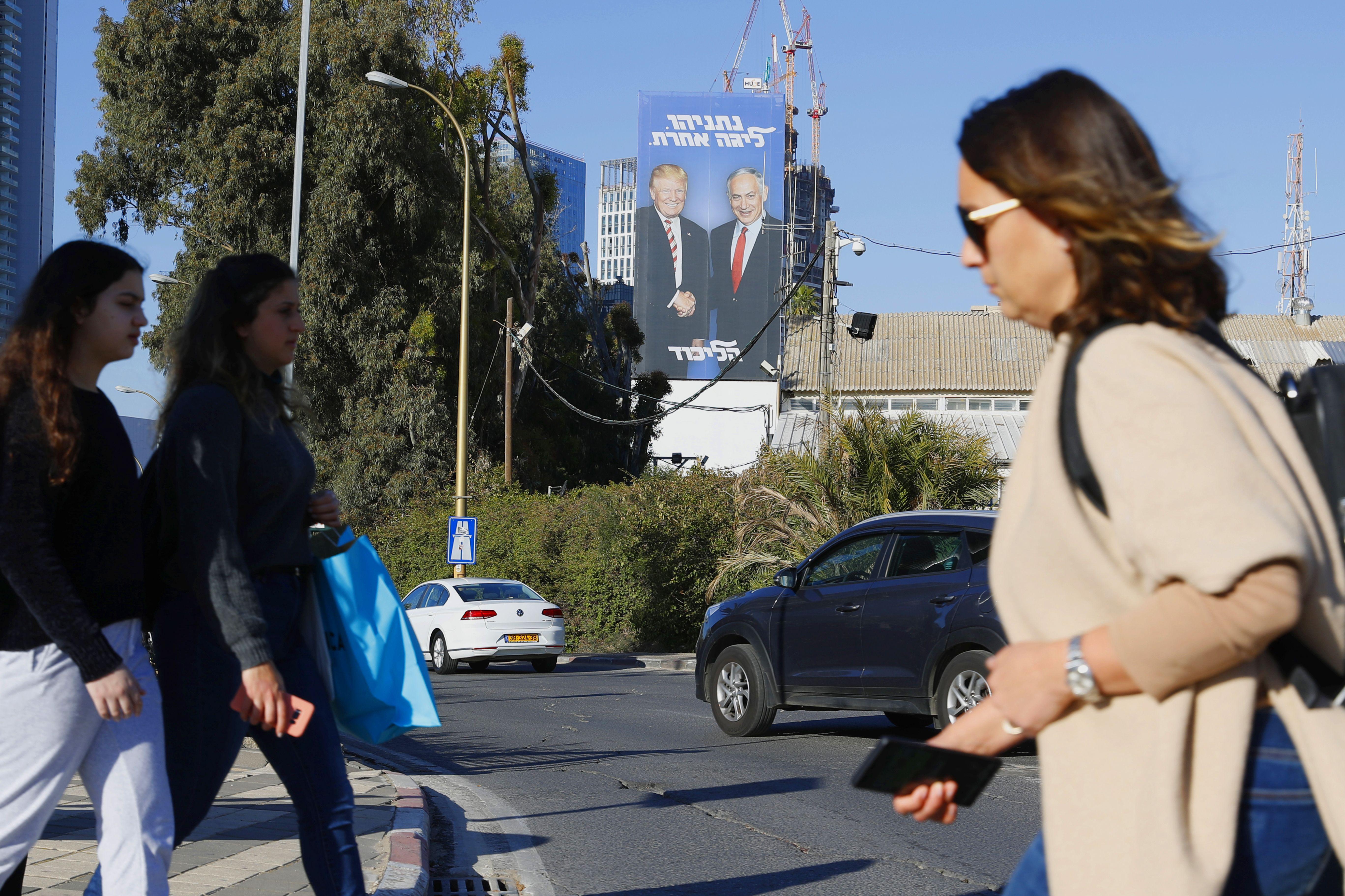 Pedestrians cross a street in front of a giant election billboard showing Israeli Prime Minister Benjamin Netanyahu and U.S. President Donald Trump shaking hands, in the Israeli coastal city of Tel Aviv on Feb. 3