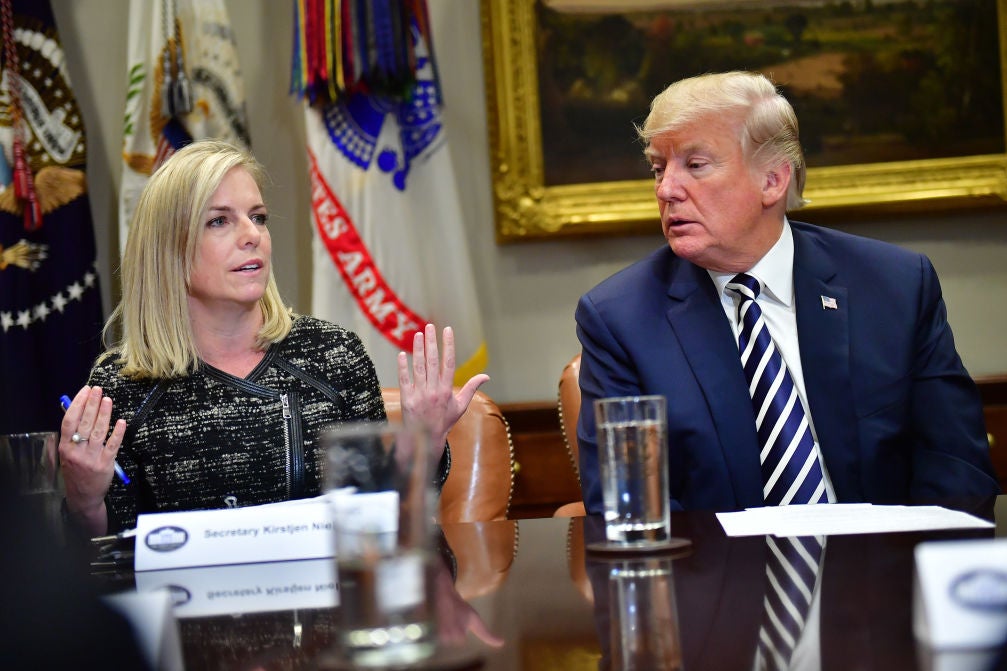 Nielsen gestures as Trump looks on while both are seated at a roundtable-style event.