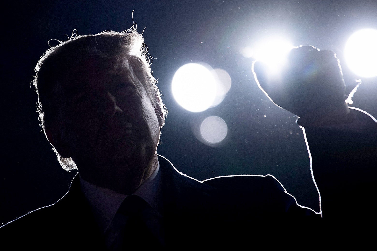 Donald Trump against a dark night sky with large flood lights behind him.