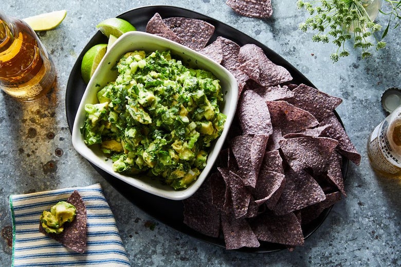A bowl of guacamole with purple tortilla chips.