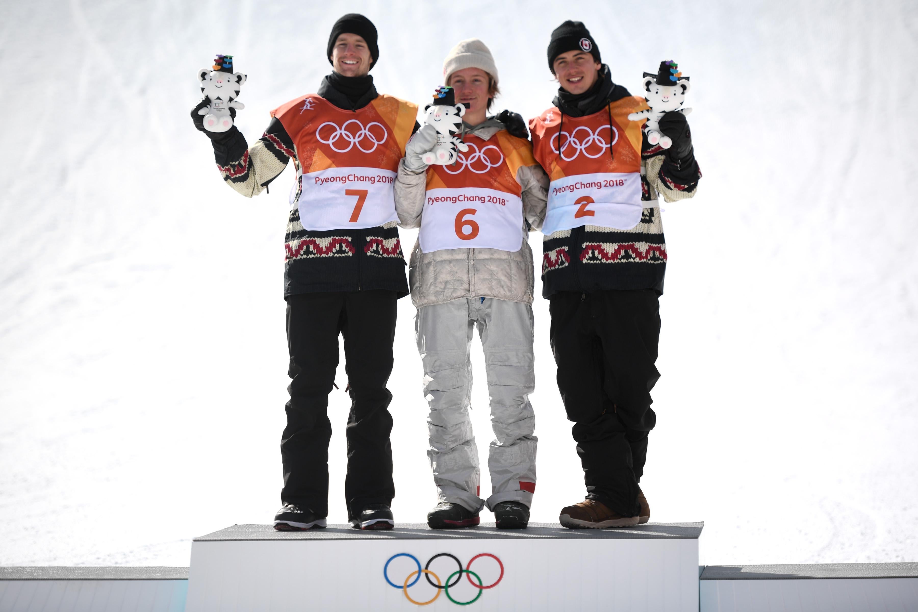 The three slopestyle medalists stand on the podium and hoist their stuffed tigers into the air.